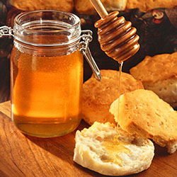 Jar of honey with honey dipping stick pouring honey on a biscuit.