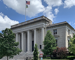 A white square building with pillars and an American flag.