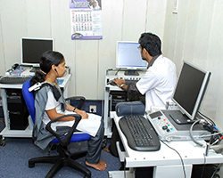 A girl sits in a chair while her doctor looks at his computer.