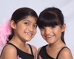 Two young twin girls in dance uniforms smiling.
