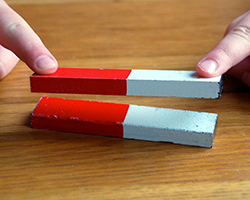 Image showing someone trying to hold a magnet down, but it is repulsed away from another magnet.