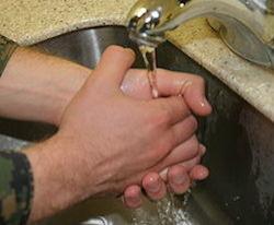 A person holds their hands in a clap-like position under a sink faucet. The person is holding their hands under the faucet in order to wash them
