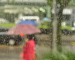 rain on a window with blurred people and umbrellas in the background