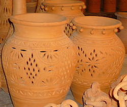 Two decorated clay pots sit in front of many others. They are orange-brown in color, and their decorated with an artistic design of small holes.