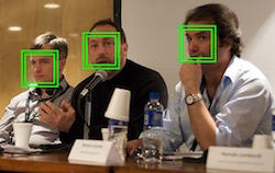 3 men are sitting at a table, but not looking toward the camera. Drinks and name badges rest on the table in front of them. Green boxes also sit on top of their faces, suggesting facial recognition process is occurring