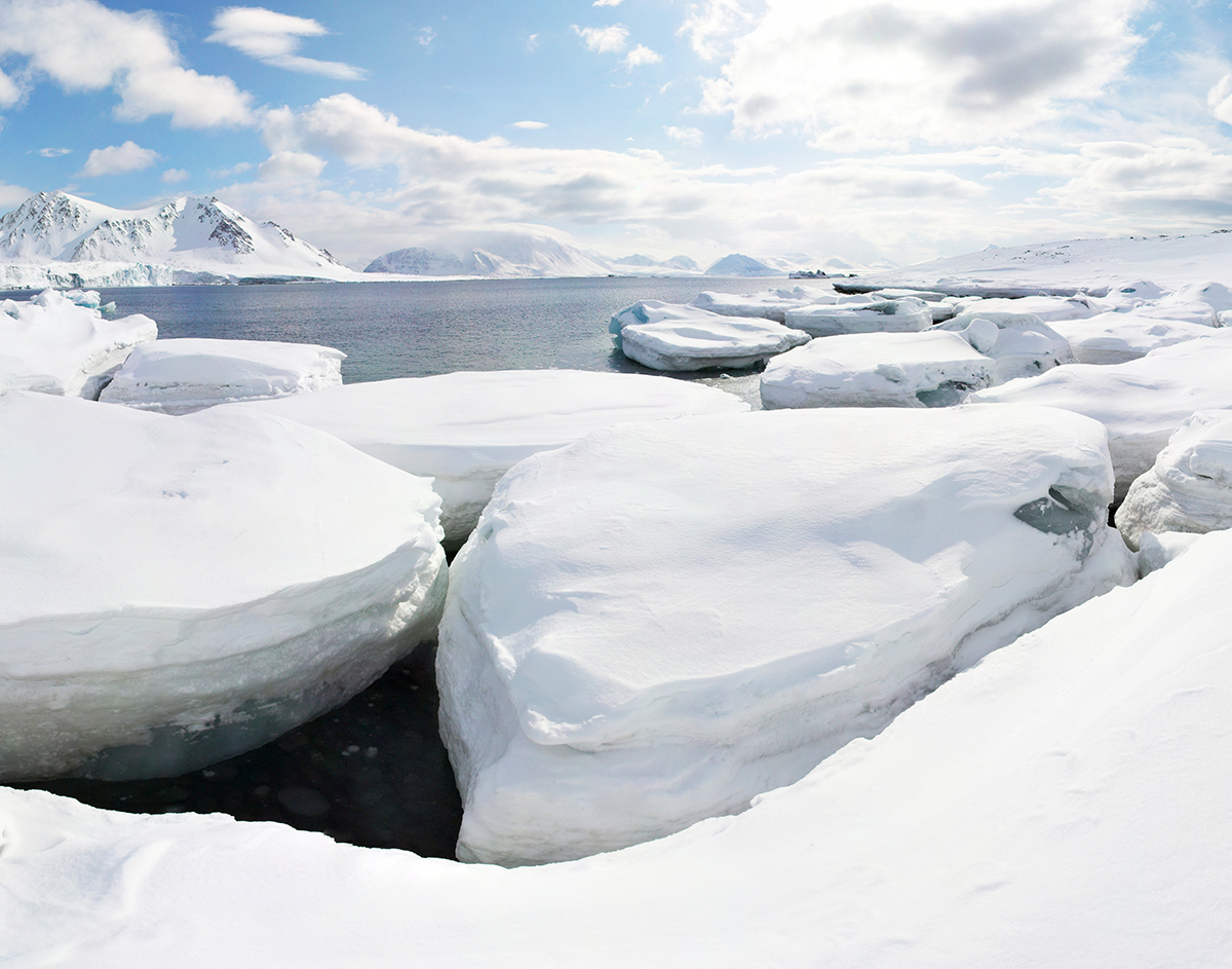 A snow covered Arctic landscape with some icebergs and the ocean in the distance. 