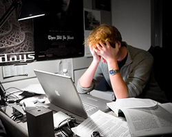A man with red hair clutching his head in frustration at his office desk.