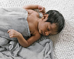 A newborn child laying under a gray blanket