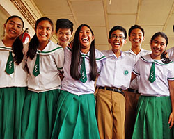 A group of students with white polo shirts and green skirts holding each other and laughing
