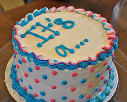 A circular white cake that reads &quot;It's a...&quot; with blue and pink dots
