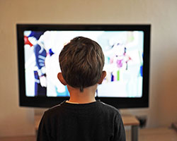 The back of a young boy's head sitting in front of a TV