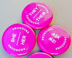 Three circular pink pins displaying different pronouns