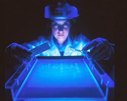 A scientist holds measuring tools over gel electrophoresis equipment