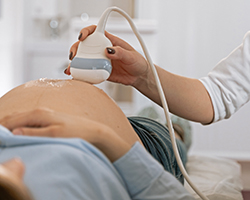 An image of a doctor holding an ultrasound device to a pregnant person's stomach.