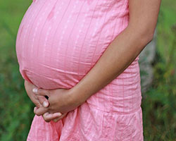 A pregnant person wearing a pink dress clutches their abdomen