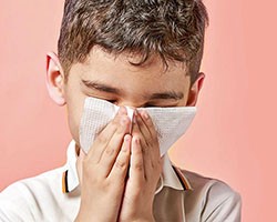 A young boy holding a tissue to his nose as he sneezes