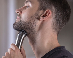 A man holds a razor against his beard, shaving.