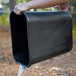 An image of someone pouring water out of a small black trash bin.