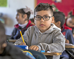 A young kid with glasses sitting in a classroom.