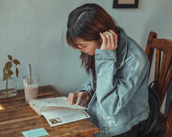 A girl in a jean jacket reading a book in a small cafe, with a drink on the table