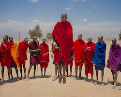 Maasai men in a half circle, in colorful clothing, with one man jumping in the middle