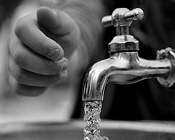A young person's hand reaching toward a faucet that has water coming out of it.