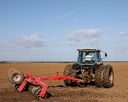 A tractor tilling (mixing up the dirt) in a farm field