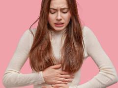 A woman clutching her abdomen, experiencing period cramps.