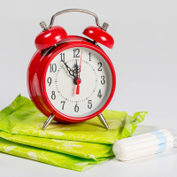 A red alarm clock sitting on top of a pile of green sanitary pads next to a tampon