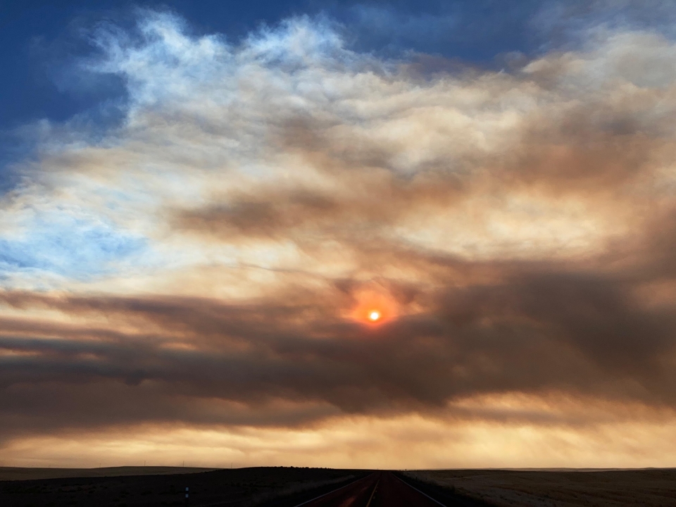 A smoky sky with a sun behind the smoke clouds on the horizon