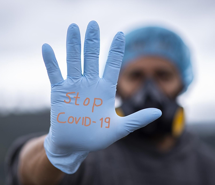 A masked person holding up a gloved hand, with "Stop COVID-19" written on the glove